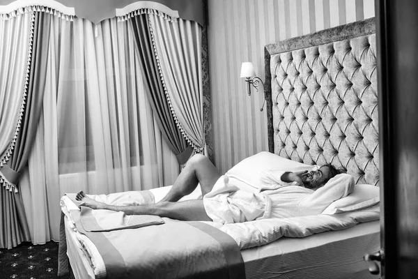 Gyönyörű szállodai szobában. Szakállas férfi ágyon a telefon — Stock Fotó