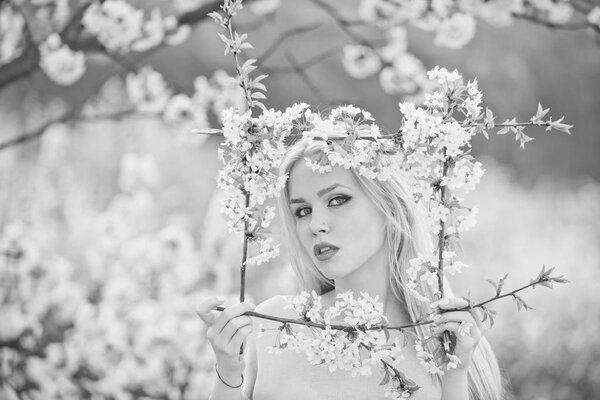 Beauty and nature. Adorable woman or cute girl with stylish makeup, blond, long hair holding frame of white, blossoming flowers in spring garden on sunny day on blurred floral environment.