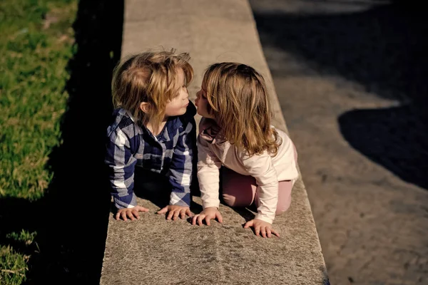 Eerste kinderlijke liefde. Jongen en meisje kussen op stenen stoeprand op zonnige dag — Stockfoto