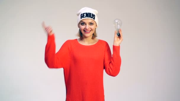 Idea y concepto creativo. Una mujer con sombrero con palabra de genio, descubrió una idea. Chica en un suéter rojo con una bombilla en la mano tiene una nueva idea . — Vídeo de stock