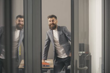 Modern ofis cam duvarlı mutlu bir iş adamı. Sakallı adam oda kapı dışarı bak. Kendine güvenen adam çalışma evinde rahat kıyafetli. İş ve ofis yaşam tarzı. Güven ve başarı kavramı