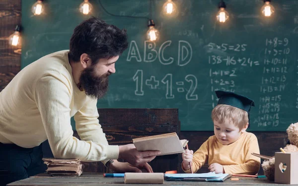 Idea prodigio e geniale. Padre, insegnante lettura libro, insegnare bambino, figlio, lavagna su sfondo. Il ragazzo con il cappello da laureato ama ascoltare papa '. Papà vuole crescere geniale figlio — Foto Stock