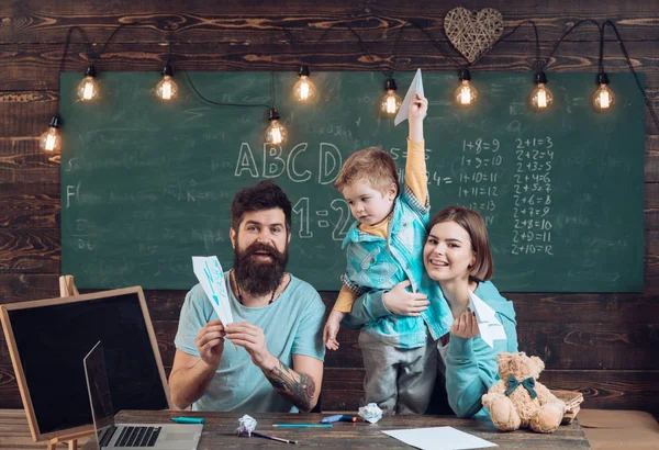 American family at desk with son play with paper planes. Homeschooling concept. Parents teaching son american traditions playing. Kid with parents in classroom with usa flag, chalkboard on background — Stock Photo, Image