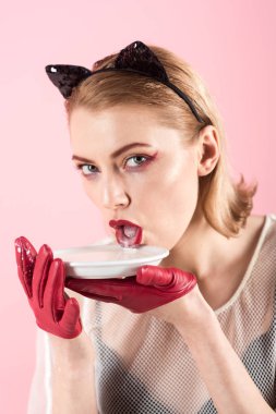 Kız yavru kedi kulakları ve yoğurt pembe bir arka plan üzerinde kırmızı eldivenler. Diyet ve sağlık. Kedi kadın ye ekşi krema. Ekoloji ürün ve heath. Seksi kedi kadın yalamak süt plaka. Yiyecek ve içecek.