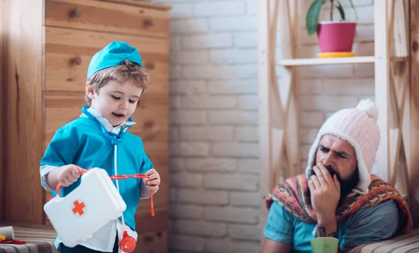 Hello I am your doctor. Son with first aid box take care of father at home. Little child play doctor with man. Boy in doctor uniform treat patient. Medicine and health. Game and development — Stock Photo, Image