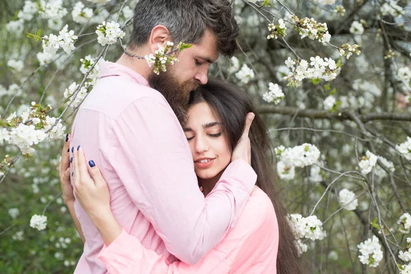 Sentirsi calmi e protetti. Pelle e freschezza. San Valentino. Uomo barbuto abbraccio donna sensuale. Coppia innamorata tra alberi in fiore. Amore e romanticismo. La primavera è la stagione dell'amore — Foto Stock