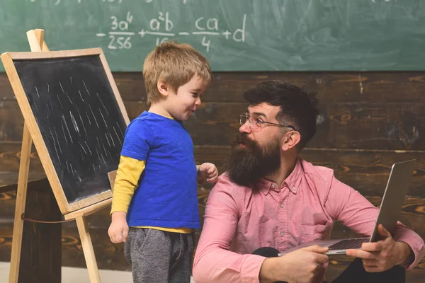 Vater und Sohn im Klassenzimmer. Mann und Kind schauen sich belustigt an. Mann im rosa Hemd sitzt mit Laptop auf dem Boden — Stockfoto