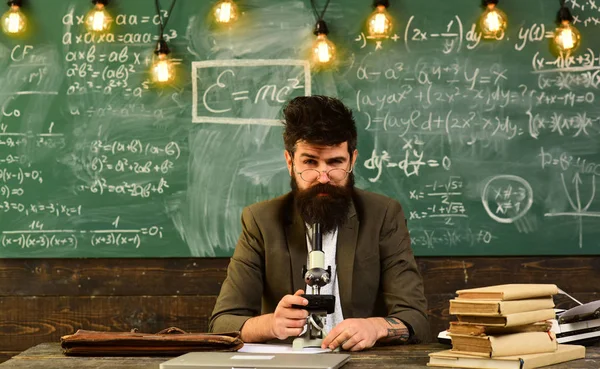 Empresario con gafas e instrumento óptico en escritorio. El hombre barbudo trabaja con el microscopio. Hombre con barba y bigote en la escuela. Los científicos investigan en pizarra. Ciencia y estudio —  Fotos de Stock