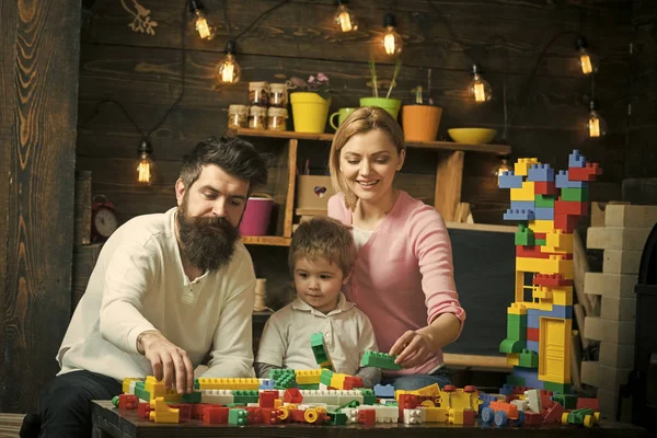 Familie fritid. Dreng med forældre leger med plastblokke, bygger byggeri. Far, mor og søde søn lege med konstruktør mursten. Familie på travle ansigter tilbringer tid sammen i legerum. Familie - Stock-foto