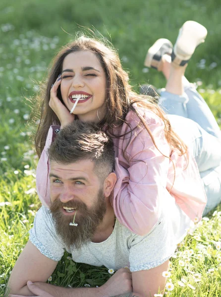 Känna sig fri och avslappnad. Lyckliga par i kärlek. Kvinnan röker cigarett liggande på mannen med daisy i munnen. Par koppla av på grönt gräs. Njuta av sommarlovet — Stockfoto