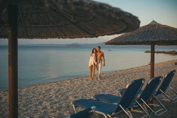 Aşk Denizi Adası'nda şemsiyelerle sahilde günbatımı yürüme çift. — Stok fotoğraf