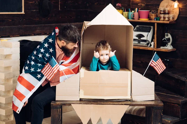 Patriotismo y libertad. Viaje y aventura. Familia e infancia. Padre y niño pequeño en un cohete de papel con bandera americana. Feliz día de la independencia de los EE.UU. Sueño con la carrera del cosmonauta —  Fotos de Stock