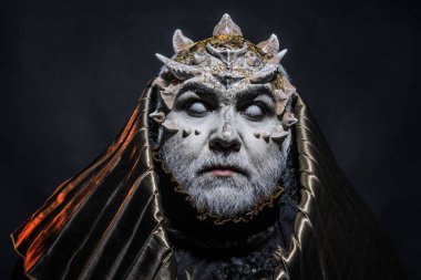 Beyaz sakallı komuta sizde canavar gibi giyinmiş. Adam dikenler veya siğiller ile yüz pırıltılar ile kaplı. Siyah zemin üzerine altın kukuleta ile iblis. Fantezi kavramı. Uzaylı, iblis, büyücü makyaj