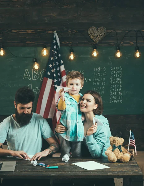 Amerykańska rodzina turystycznej z synem Dokonywanie samoloty papieru. Rodziców, uczy syna amerykańskiej tradycji gry. Dziecko z rodzicami w klasie z flagą usa, tablica na tle. Koncepcja domu — Zdjęcie stockowe