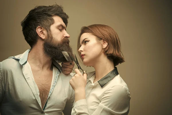 Дівчина моди краси. Модний вигляд. Жінка-перукар розрізає бороду ножицями. Чоловік з довгою бородою, вусами і стильним волоссям, світлим тлом. Барбершоп або перукарська концепція — стокове фото