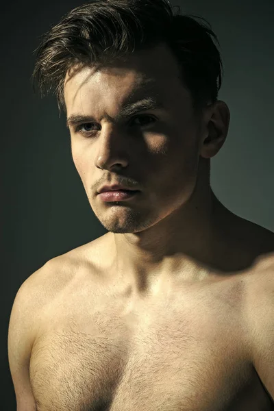 male fashion portrait. Macho on pensive face with muscular figure, sportsman, bodybuilder. Man with torso, muscular macho, shadow on body, dark background. Guy with tattoo looks confident and