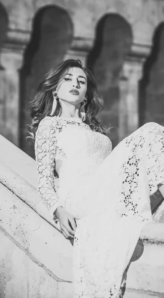 美女时尚模特女孩时尚的外观。穿白色连衣裙的女孩坐在旧石头扶手上 — 图库照片
