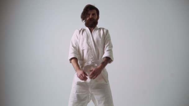 Komik karate avcı beyaz kimono giymiş. Ellerini sallayarak ve kendini kasığından yenerek garip karate — Stok video