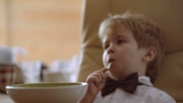 Niño alegre en la cocina comiendo gachas y ver dibujos animados — Vídeos de Stock
