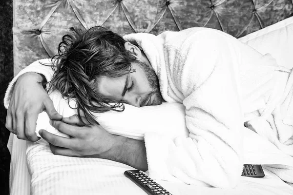 Concetto di stanchezza. uomo barbuto sul letto con telecomando — Foto Stock