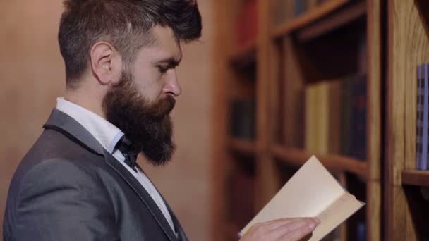 남자는 책장에 책 서를 읽습니다. 평온한 얼굴로 성숙한 남자는 독서를 즐긴다. 라이브러리 개념. — 비디오