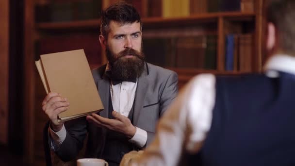 Man presenteert een boek naar zijn collega in de bibliotheek. Literaire figuren. Onderwijs en studeren concept. — Stockvideo