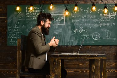 Kara tahta üzerindeki bir bilgisayarla uzun sakallı adam. Sakallı adam iş laptop sınıfta. Takım elbise kullanım defter okul masasında iş adamı. Gözlük dahi yüzünde bir bilim adamı. Yeni teknoloji kavramı