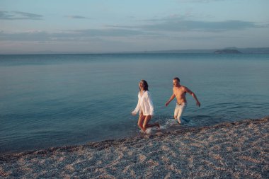 İki aşık deniz ya da okyanus plaj su sıçrama içinde çalıştırın. Özgürlük kavramı. Kadın erkek gömlek ve deniz dalgalar halinde çalışan giyer. Dostum kadar yakalar kadınla, oyna, eğlen