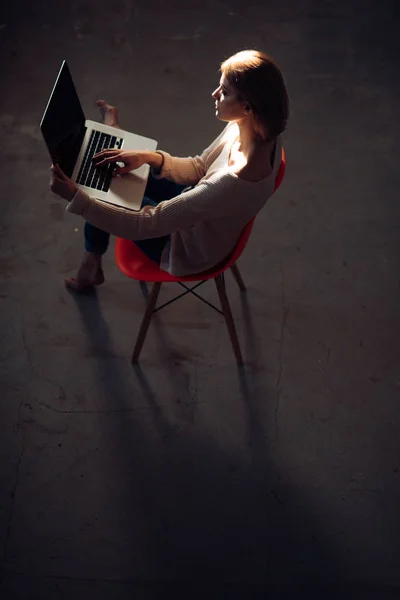 Mi godo il tempo a casa. Bella giovane donna che lavora su laptop seduta su una comoda sedia a casa . — Foto Stock