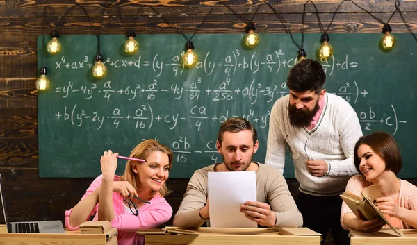 Estudiantes, compañeros de grupo hablando, pidiendo consejo, explica el profesor. Profesor barbudo, profesor, profesor de enseñanza, pizarra en el fondo. Estudiar el concepto de dificultades —  Fotos de Stock