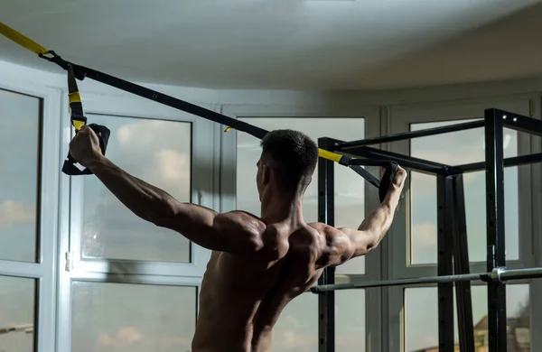 Mann mit Oberkörper, Sportler, Athlet, muskulöser Macho trainiert mit Trx-Schlaufen, Fenster im Hintergrund. Sport- und Fitnessstudio-Konzeptmann mit nacktem Oberkörper und muskulösem Rücken im Fitnessstudio genießt das Training, trxs — Stockfoto