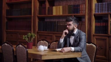 İşadamı vintage iç oturur, kitap ve çay almıştır. Onun dolabında lüks elbiseli sakallı adam. Lüks yaşam tarzı, vintage moda, çay kavramı.