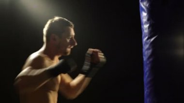 Sakallı erkek boxer koyu arka planda kum torbası ile eğitim. Kum torbası eğitim genç boksör. Erkek boksör olarak egzersiz için büyük mücadele. Boksör sayısı kum torbası.