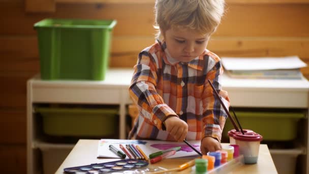 Маленький мальчик рисует пальчики на белой бумаге с улыбкой. Счастье в творчестве — стоковое видео