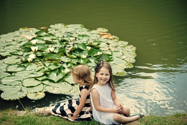 Conceito de férias de verão. Meninas sentar-se na grama na lagoa com flores de lírio de água — Fotografia de Stock