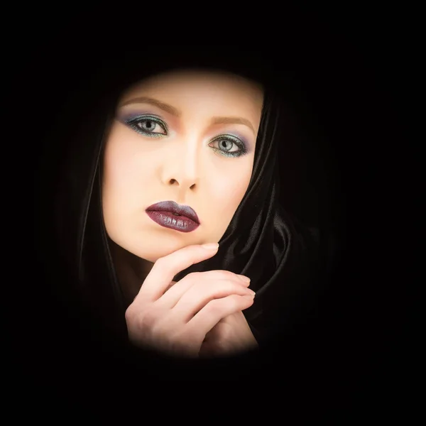 Retrato de uma senhora bonita vestindo um manto com capuz preto gótico. pose contra um fundo preto — Fotografia de Stock