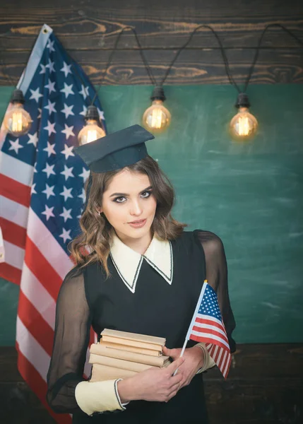 Estudiante inglesa con la bandera americana al fondo. Concepto de educación estadounidense. Grupo de estudiantes con bandera de Estados Unidos en el campus universitario —  Fotos de Stock