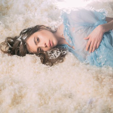 Güzel kız tüyler ortasına yatakta yatan ve kameraya bakıyor. Kadın ihale pijama rahatlatıcı. Hafiflik kavramı. Şeffaf mavi Geceliği Bayan tüy yığını yatakta yatıyordu