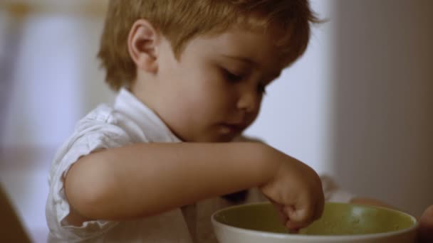 Pojken äter gröt. Barn äter gröt samtidigt titta på tecknad film. barn självständighet koncept — Stockvideo