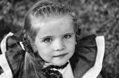 Samimi çocuk fotoğraf makinesine benziyor. Mutlu sevimli kız örgü saçlı yeşil çimenlerin üzerinde gülümseyen