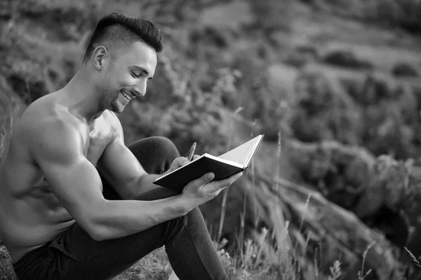 Ελκυστική gay διαβάζει ένα βιβλίο. Χαμογελώντας μυώδης άνδρας με βιβλίο εξωτερική — Φωτογραφία Αρχείου