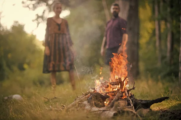 Couple is resting by the fire. Man and woman on blurred background look at fire flame — Stock Photo, Image