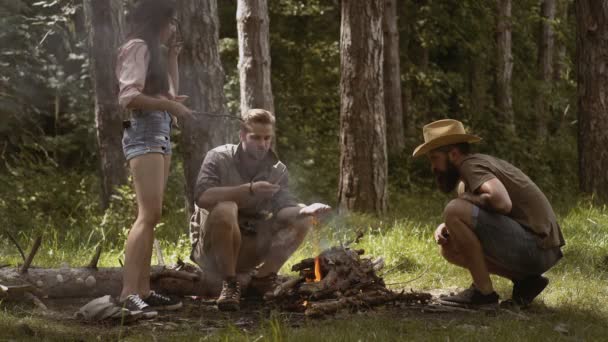 Amigos felices disfrutando de la hoguera en la naturaleza. Amigos asando malvavisco dulce en un fuego por la noche en el bosque — Vídeos de Stock