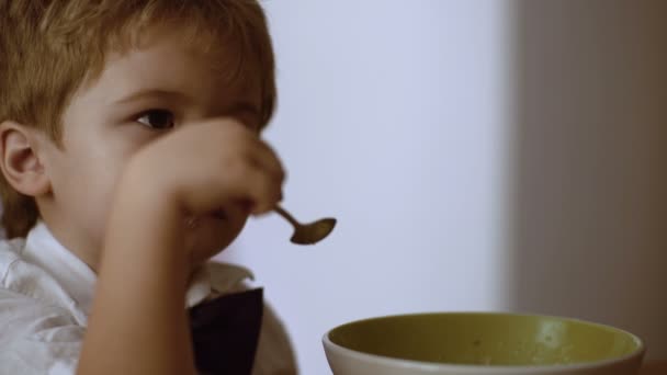 Gyermek függetlenség fogalma. Fiú eszik a kását. Gyerek eszik a kását közben Nézd meg a rajzfilmeket — Stock videók