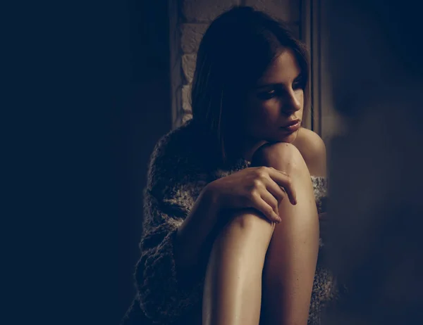 Sola con sus pensamientos. Mujer sentada con piernas en el alféizar de la ventana. Mujer joven con maquillaje y cabello largo. Chica de belleza con aspecto de moda. Soñando en su imaginación. Cuidado de la piel y belleza de la piel — Foto de Stock