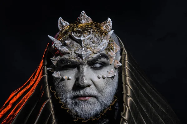 Beyaz sakallı komuta sizde canavar gibi giyinmiş. Adam dikenler veya siğiller ile yüz pırıltılar ile kaplı. Fantezi kavramı. Siyah zemin üzerine altın kukuleta ile iblis. Uzaylı, iblis, büyücü makyaj