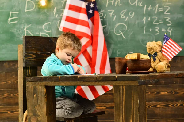 Amerikanischer Vorschüler zeichnet oder schreibt in der Nähe der US-Flagge. — Stockfoto