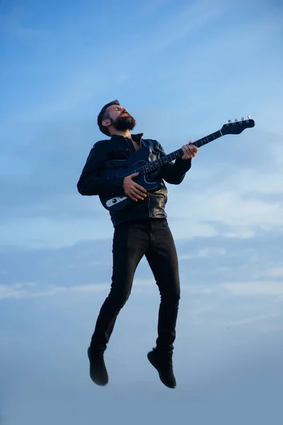 A música e a liberdade fazem-no feliz. Música, hipster barbudo tocar guitarra voando no céu azul — Fotografia de Stock