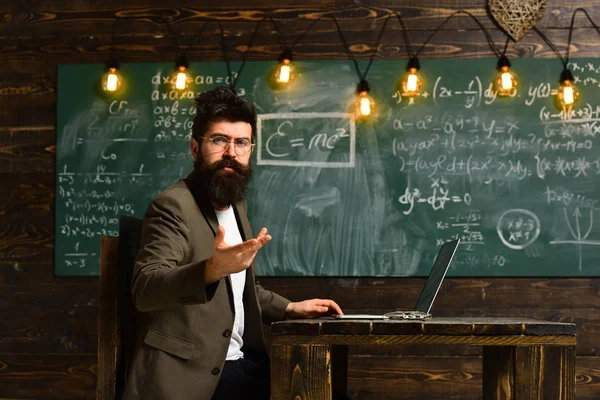 Hombre con barba larga trabajando en la computadora en pizarra. El hombre en el traje a la moda usa el portátil en el escritorio de la escuela, el concepto de nueva tecnología —  Fotos de Stock