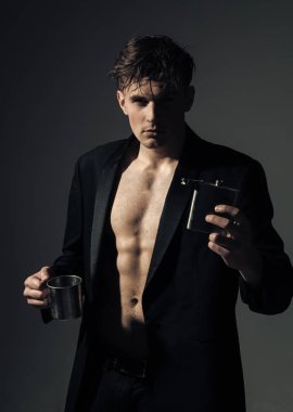 Lüks alkol kavramı. Adam kendinden emin yüz, kas şekil, şişesi ile alkol ve metalik Kupası tutar. Kas gövde, altı paketleri, adamla klasik ceket giyer, çekici, koyu arka plan görünüyor.